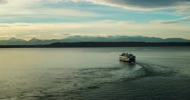 Wide aerial shot of ferry boat cruising across water with mountains in background