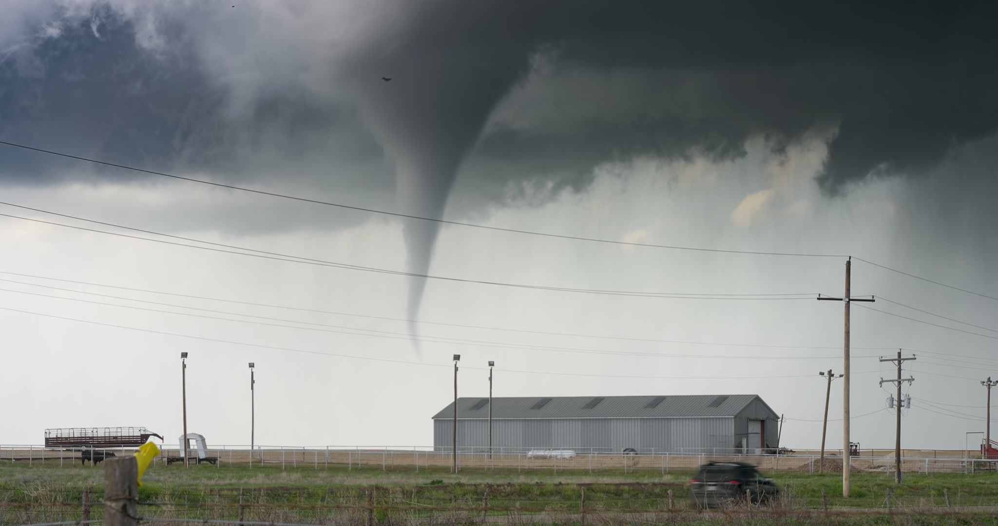 Texas Twister! Classic tornado passes behind farm as storm chaser drives by, South Plains, Texas, 4K. Cinematographer: Martin Lisius.
