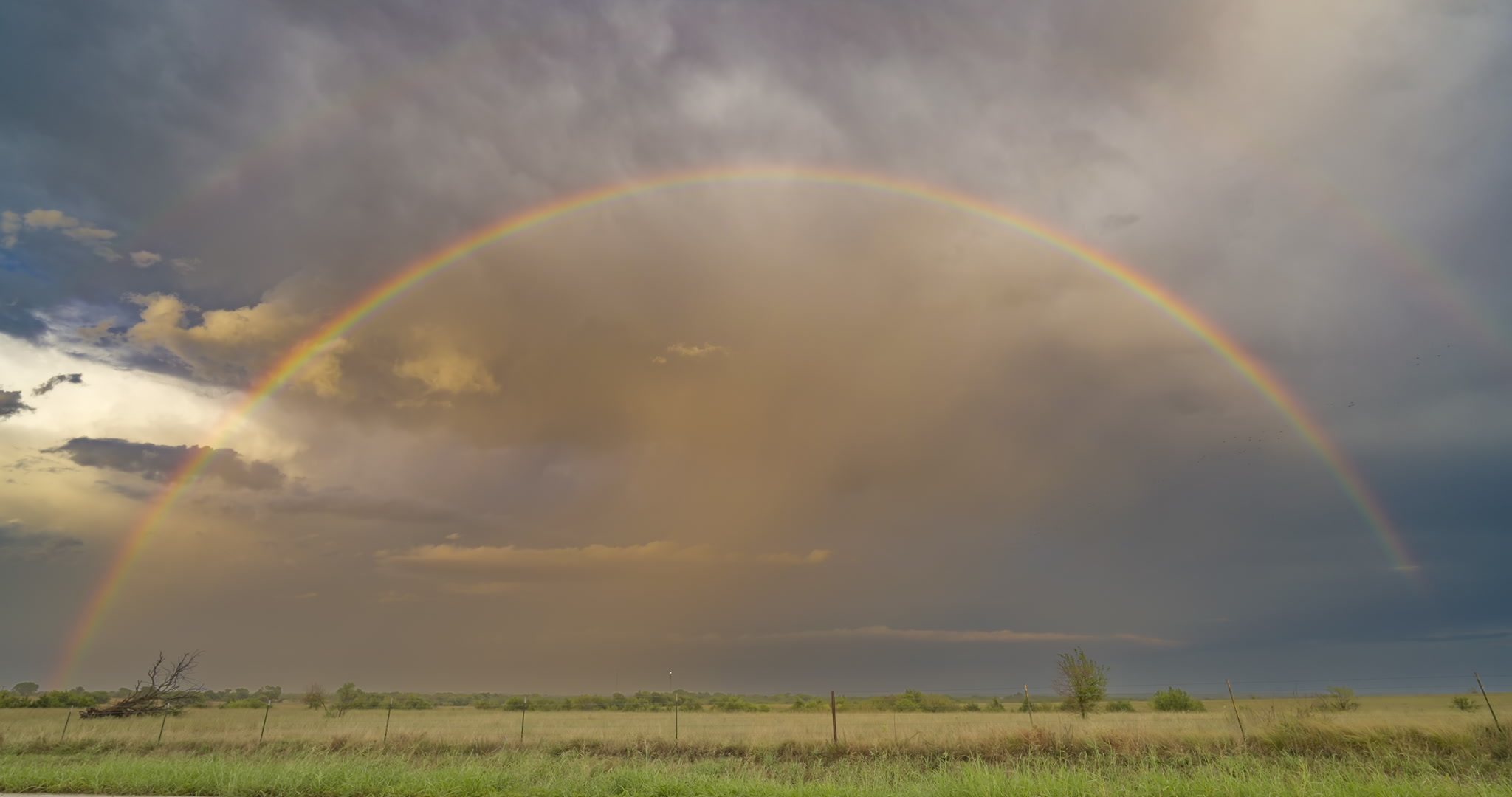 Full rainbow over green prairie, stormy sky, real-time. DCI 4K.