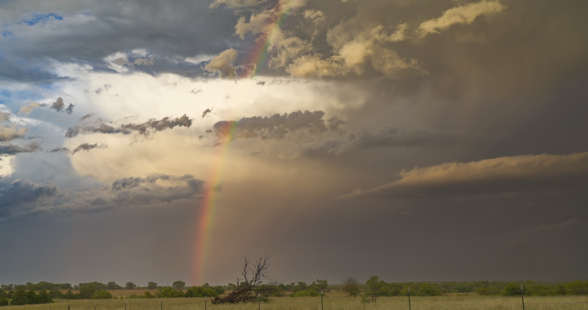 Rainbow and storm clouds over green prairie, real-time. DCI 4K.