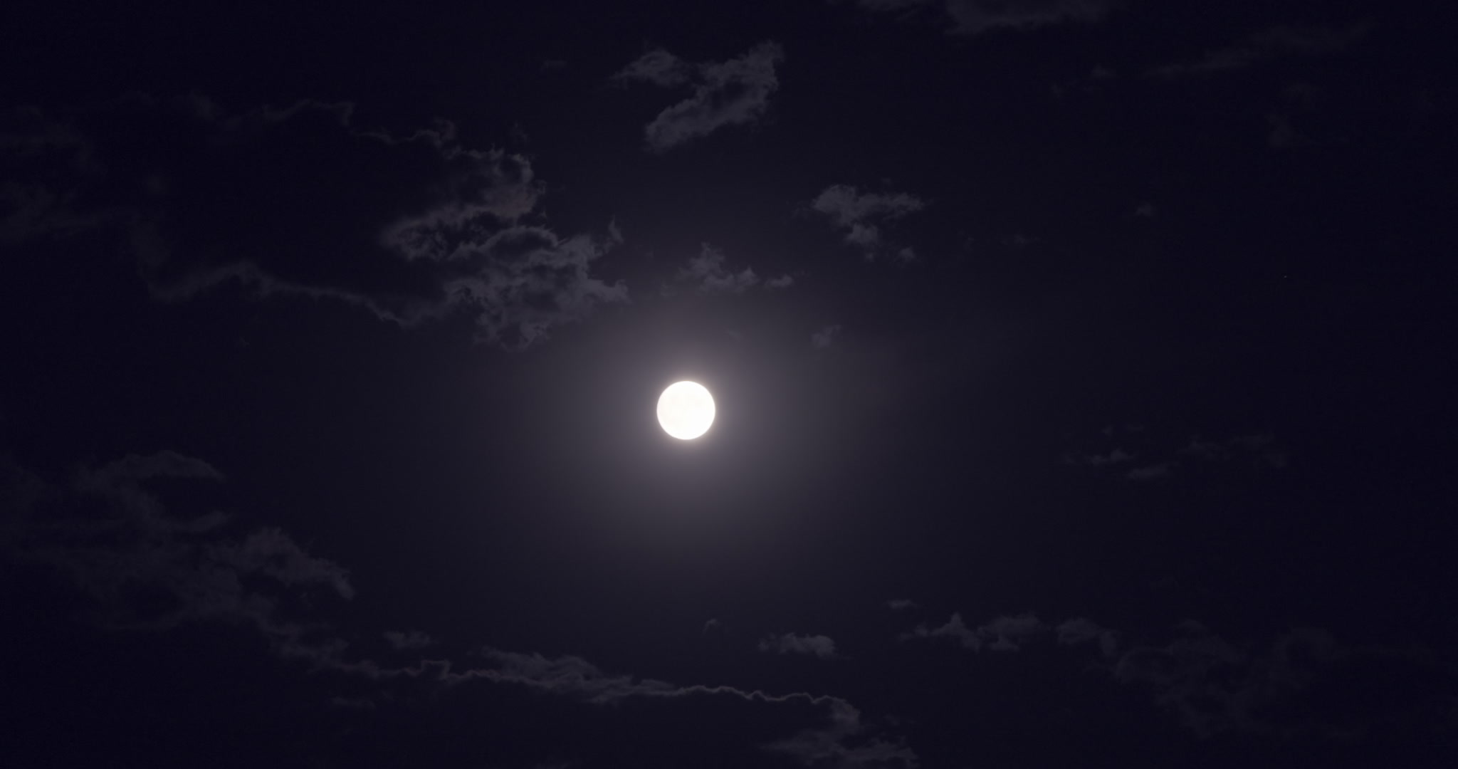 Bright, yellow full moon in dark sky with clouds drifting by. DCI 4K.