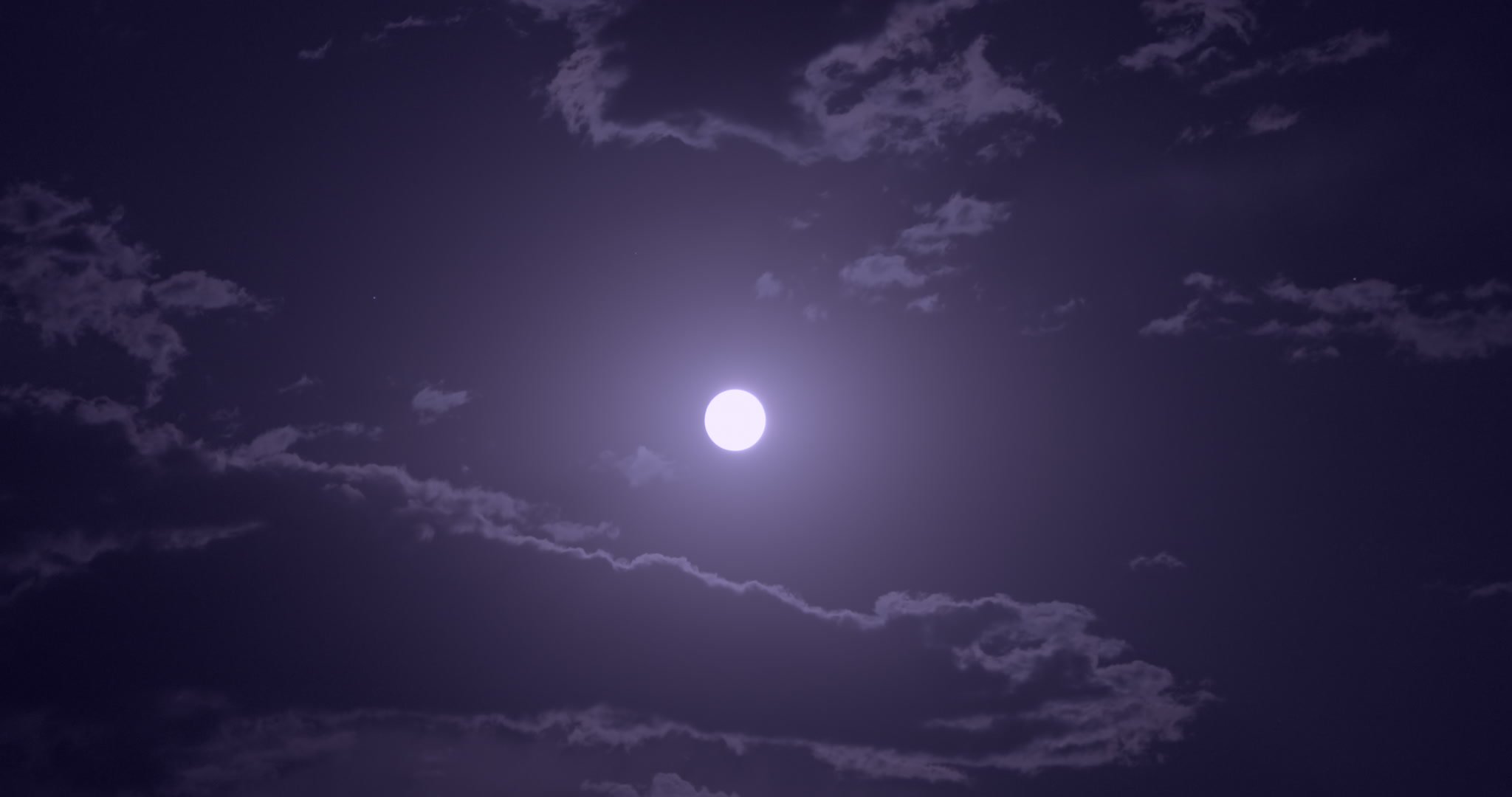 Full moon appears from behind clouds, bright, blue sky at night. DCI 4K.