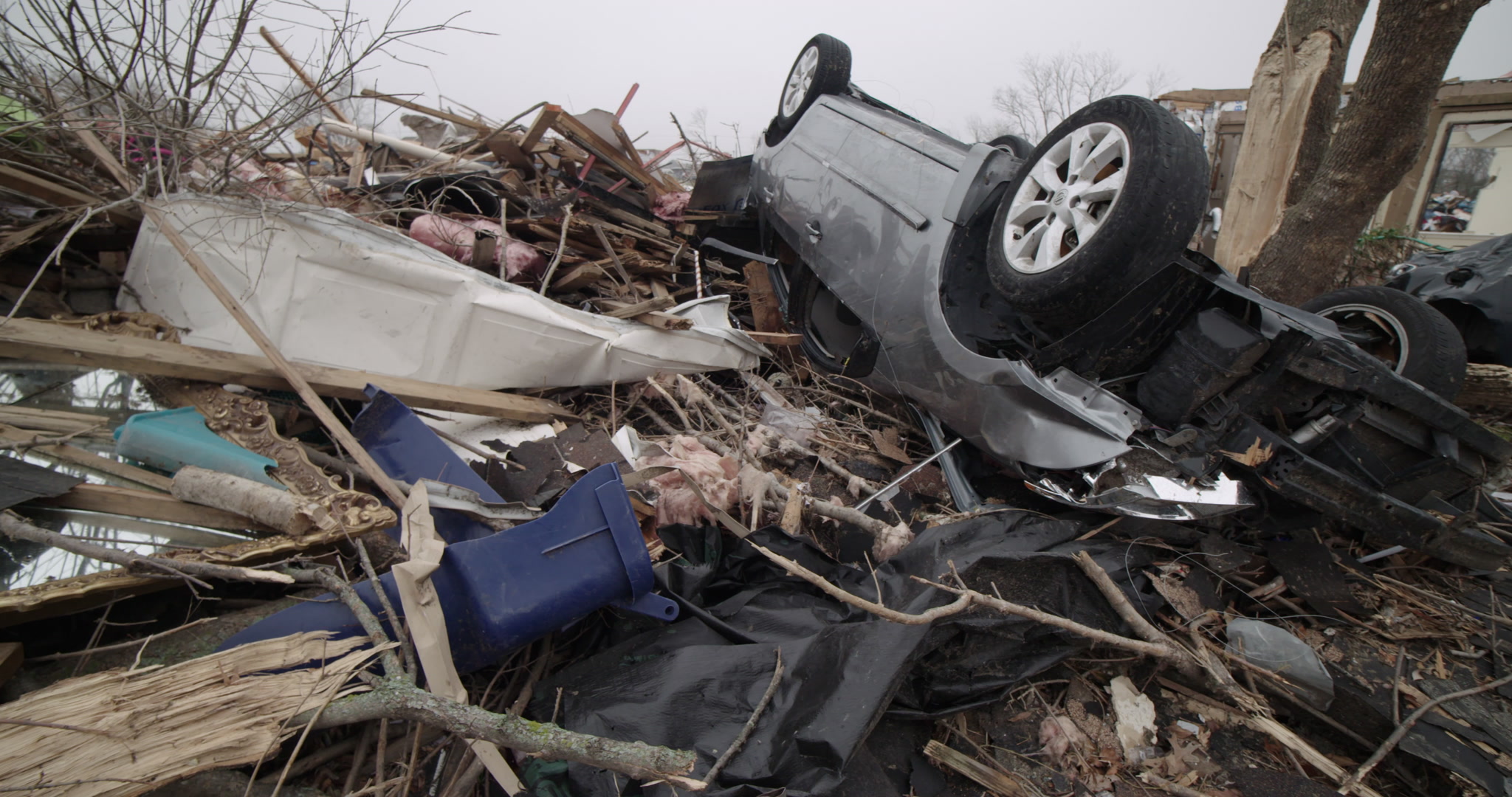 Tornado damage and aftermath - Close-up pan of upside down car on debris pile, 4K.
