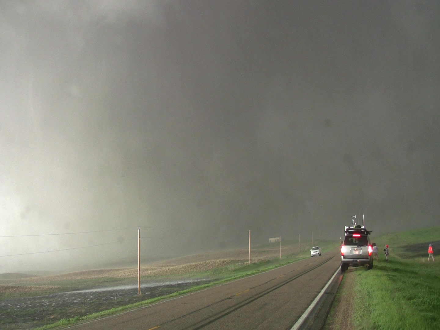 Tornado - massive tornado crosses highway, storm chaser parked right side.
